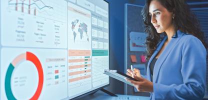 clinical - woman looking at big monitor with data - blue lab coat
